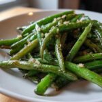 A close-up of bright green beans tossed with minced garlic and parmesan, ready to serve.