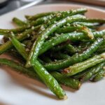 Close-up of bright green beans tossed with minced garlic and Parmesan cheese, ready to eat.