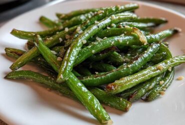 Close-up of bright green beans tossed with minced garlic and Parmesan cheese, ready to eat.