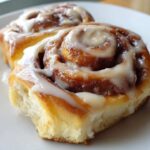 Close-up of a soft, freshly baked cinnamon roll drizzled generously with white cream cheese icing.