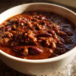 Close-up of a steaming bowl of rich, meaty crockpot chili filled with kidney beans.