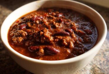 Close-up of a steaming bowl of rich, meaty crockpot chili filled with kidney beans.