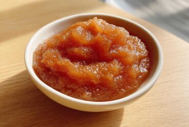 Close-up of chunky, caramelized homemade applesauce served in a small white bowl on a wooden surface.