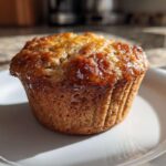A single, golden-brown honey bran muffin with a sticky, glazed top sitting on a white plate.