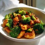 Close-up of glossy, saucy chicken and bright green broccoli florets in a white bowl, featuring honey garlic chicken and broccoli.