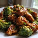 Close-up of crispy chicken pieces coated in glossy honey garlic sauce mixed with bright green broccoli florets.