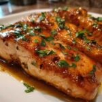 Close-up of two glazed honey garlic salmon fillets resting in sauce and topped with fresh parsley.