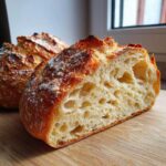 Close-up of a freshly baked Italian bread loaf cut in half, showing an open, airy crumb structure.