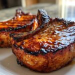 Close-up of two thick, bone-in pork chops glistening with a dark glaze, prepared using the amazing marinade for pork chops.