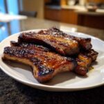 Close-up of several glazed, caramelized pork steak pieces stacked on a white plate.