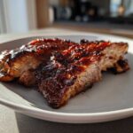 Two thick slices of a perfectly cooked, juicy pork steak recipe with a dark, caramelized glaze served on a white plate.