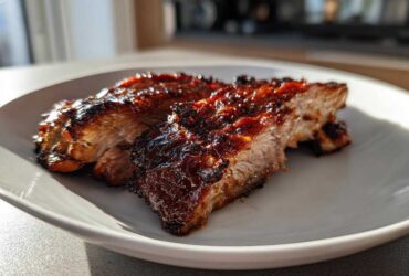 Two thick slices of a perfectly cooked, juicy pork steak recipe with a dark, caramelized glaze served on a white plate.