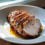 Close-up of four thick slices of perfectly cooked pork loin roast resting in its juices.