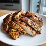 Close-up of sliced, juicy greek chicken breasts seasoned heavily with herbs and showing a perfect sear.