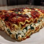 Close-up of a thick slice of lasagna with cottage cheese, spinach, and rich tomato sauce.