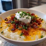 A hearty bowl of Loaded Baked Potato Soup topped with sour cream, shredded cheddar cheese, bacon bits, and chives.