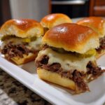 Close-up of four Mississippi pot roast sliders with melted white cheese and pickles on sweet buns.
