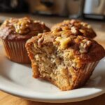 Close-up of a moist banana nut muffin, broken open to show texture, topped with walnuts.