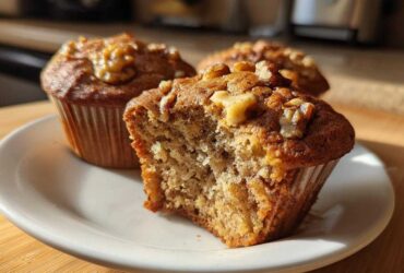 Close-up of a moist banana nut muffin, broken open to show texture, topped with walnuts.