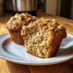 Close-up of two moist banana nut muffins, one bitten into, showing the crumb texture and walnut topping.