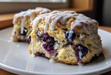 Close-up of two moist blueberry scones topped with a thick vanilla glaze, highlighting the flaky texture and burst blueberries.