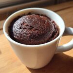 Close-up of a rich, dark chocolate mug cake freshly baked inside a white ceramic mug.