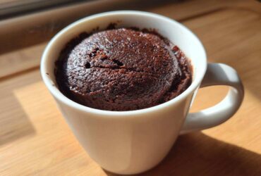 Close-up of a rich, dark chocolate mug cake freshly baked inside a white ceramic mug.