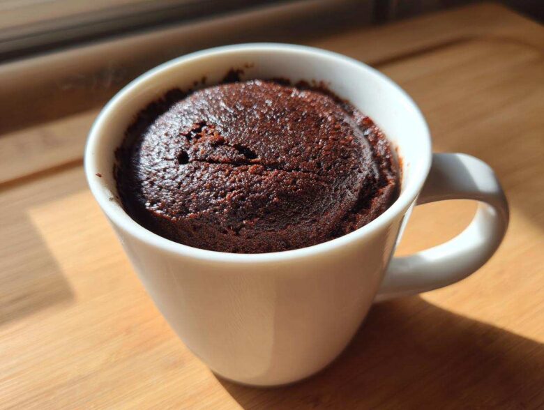 Close-up of a rich, dark chocolate mug cake freshly baked inside a white ceramic mug.