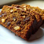 Close-up of three moist slices of dark, rich date nut bread loaded with walnuts and raisins.