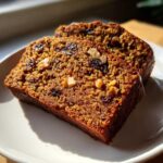 Two moist slices of date nut bread showing visible raisins and chopped walnuts baked inside, served on a white plate.