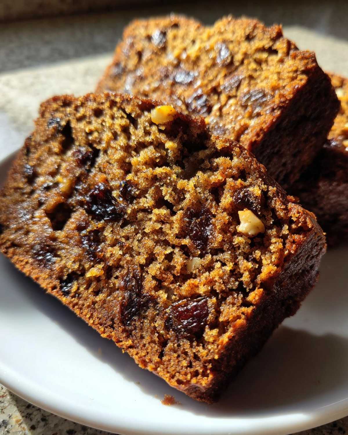 Close-up of moist date nut bread slices showing dark raisins and walnuts embedded in the rich brown crumb.