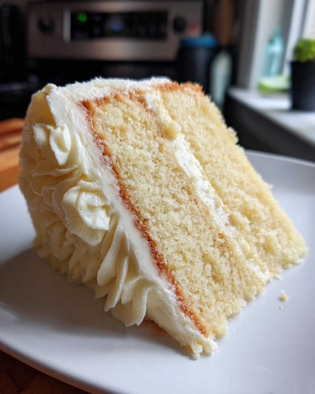 Close-up of a moist slice of vanilla cake layered with white buttercream frosting.