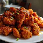 A plate piled high with crispy, glazed pieces of homemade orange chicken recipe, garnished with green onions.