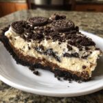 A close-up slice of rich Oreo pie showing layers of chocolate crust, pudding, and cream topping with cookie crumbles.