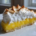 Close-up of a slice of lemon meringue pie showing bright yellow filling and perfectly toasted meringue peaks.