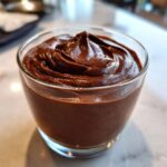 A close-up of thick, rich homemade chocolate pudding swirled beautifully in a clear glass cup.