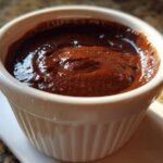 Close-up of rich, dark homemade chocolate pudding served in a white, fluted ramekin.