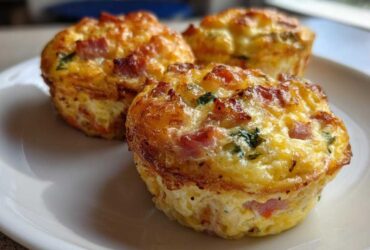 Three golden-brown, freshly baked Egg Muffin Cups with visible pieces of ham and green herbs served on a white plate.