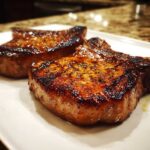Close-up of two juicy, seared pork chops showing a beautiful caramelized crust from the marinade for pork chops.