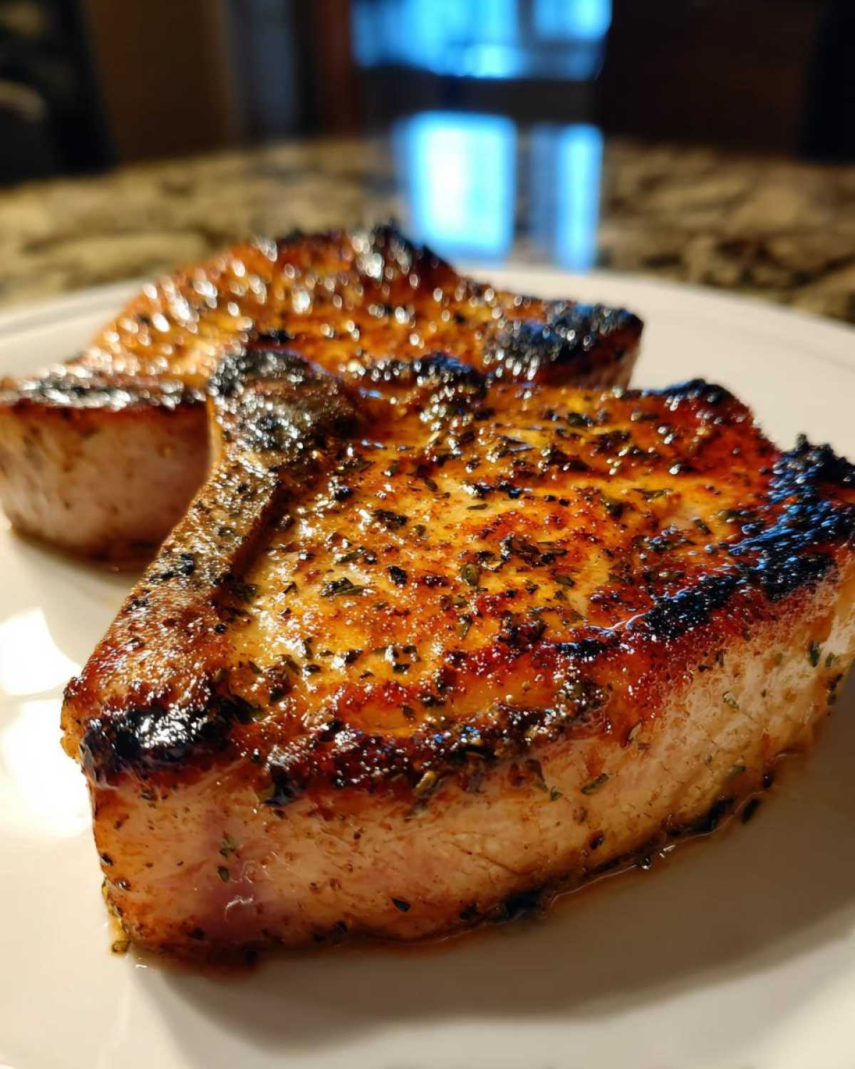 Close-up of two juicy, seared pork chops seasoned with herbs, showing the results of the marinade for pork chops.