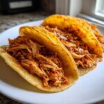 Two delicious chicken tacos filled with shredded, seasoned meat served on a white plate.