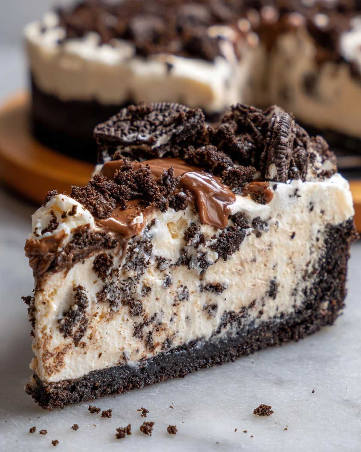 Close-up of a thick slice of creamy Oreo pie with a dark chocolate crust and cookie crumbles.