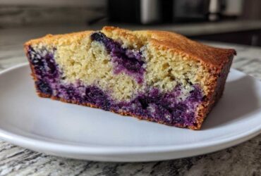 Close-up of a moist slice of blueberry banana bread showing rich purple blueberries baked into the yellow crumb.