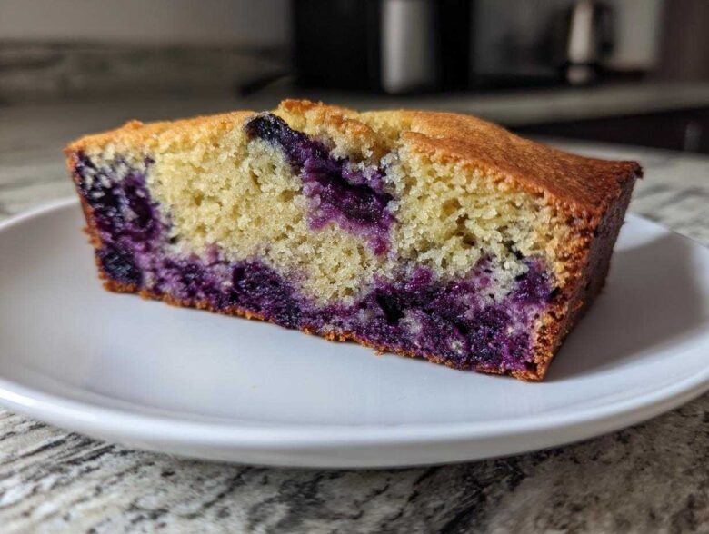 Close-up of a moist slice of blueberry banana bread showing rich purple blueberries baked into the yellow crumb.