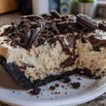 Close-up of a thick slice of creamy Oreo pie with a dark crust, topped with crushed cookies and whole Oreos.