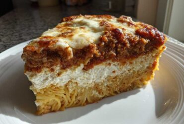 A thick slice of baked spaghetti pie showing layers of pasta, creamy filling, meat sauce, and melted cheese topping.