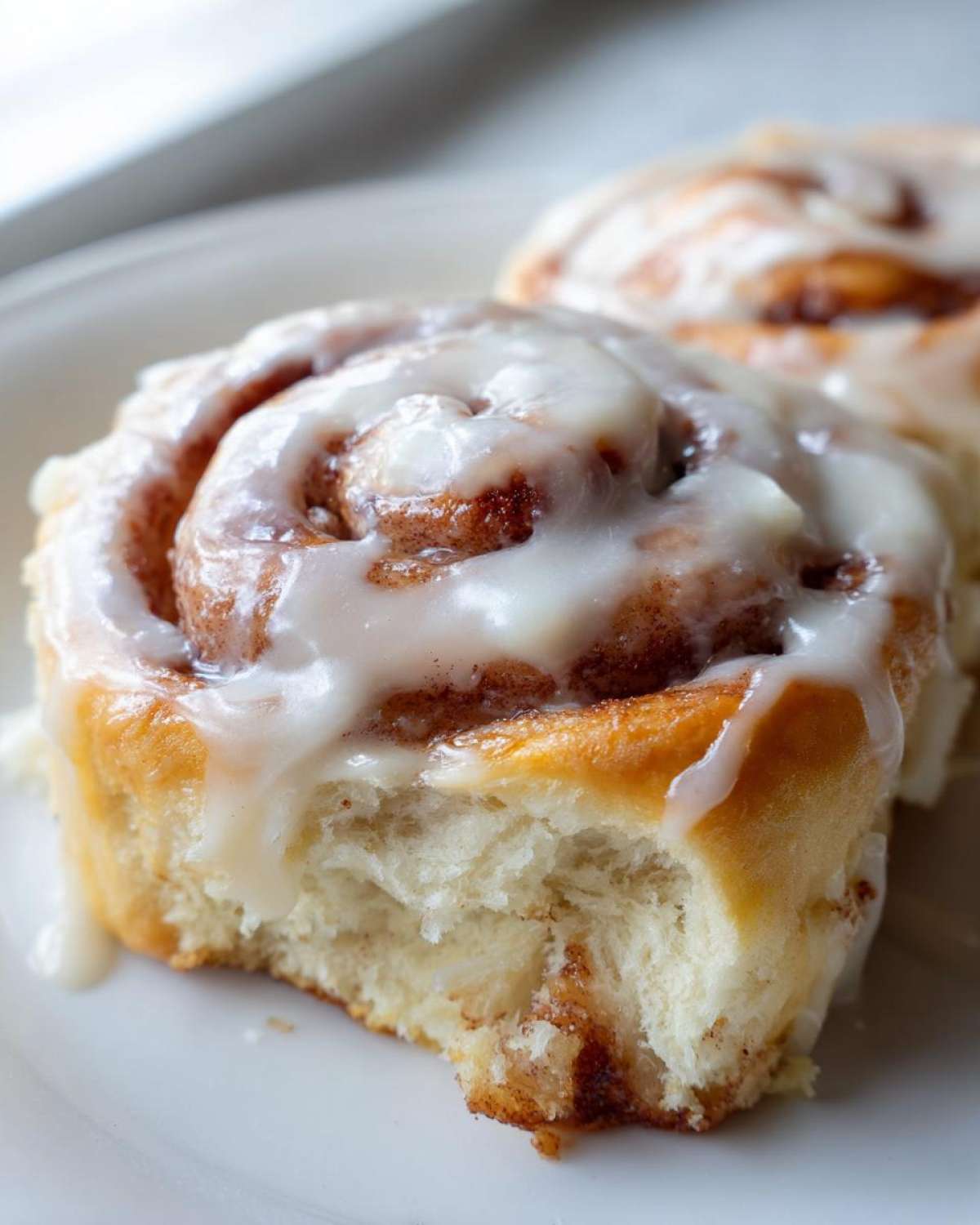 Close-up of a soft, fluffy cinnamon roll topped with dripping white icing, showing the interior texture.