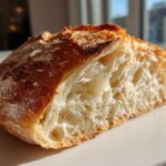 Close-up of a freshly baked french bread half showing a golden crust and airy, open interior crumb structure.
