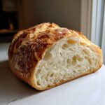Close-up of a freshly baked french bread loaf cut in half, showing the airy, soft white crumb and golden crust.