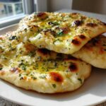 Three pieces of soft naan bread brushed with melted butter and topped with chopped parsley, resting on a white plate.